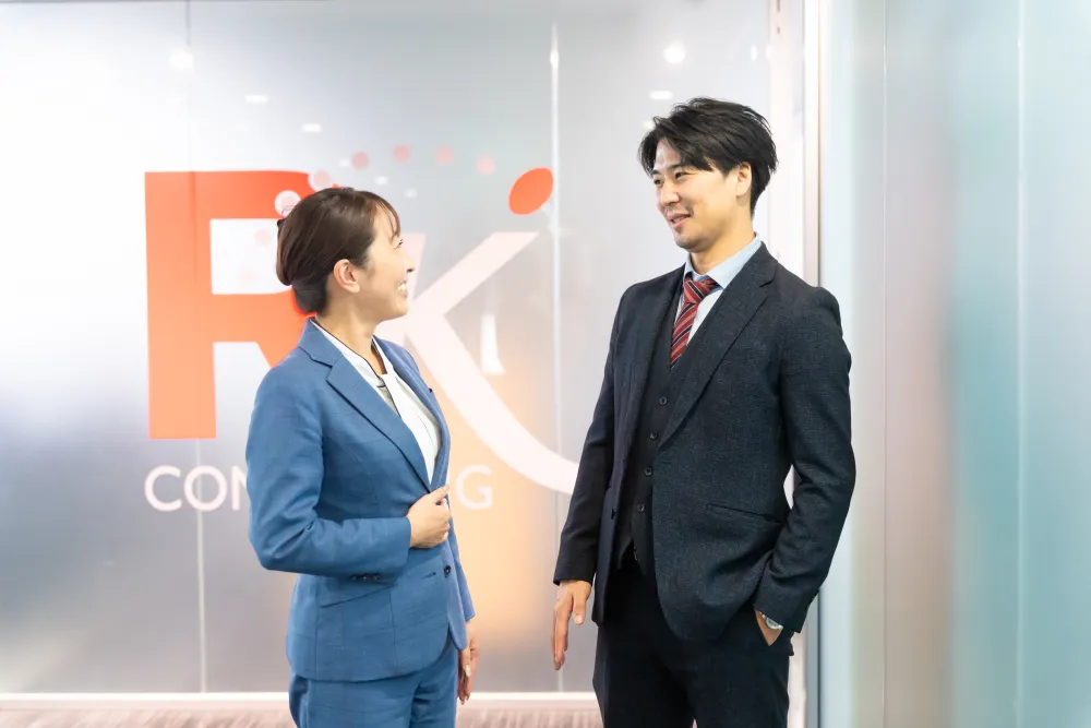 RKのロゴ前で話す紹介者と入社者